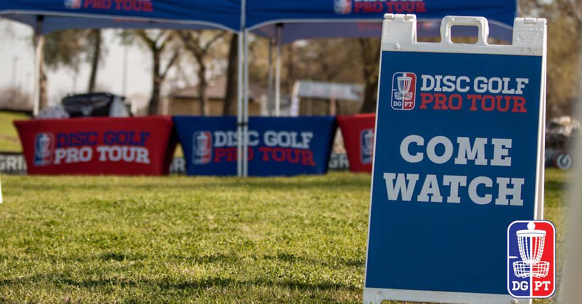 A sandwich board outdoors that says "Disc Golf Pro Tour Come Watch"