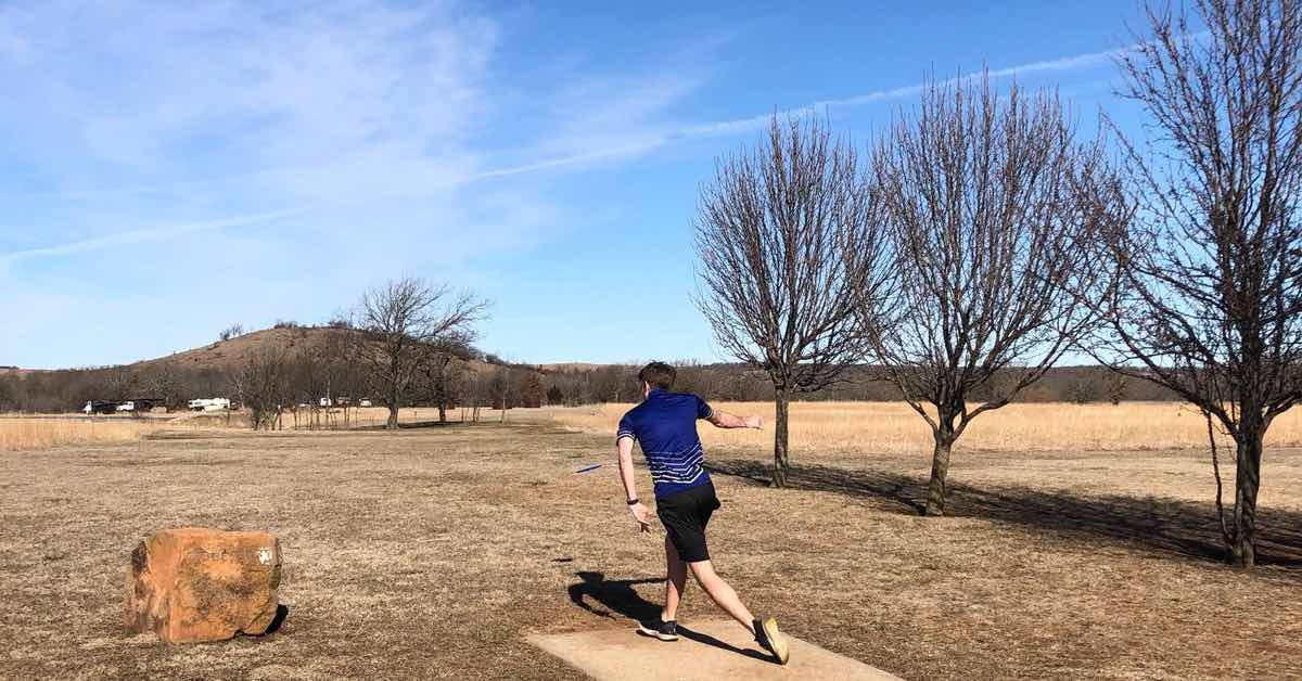 A player on a concrete disc golf tee pad throwing on a flat landscape
