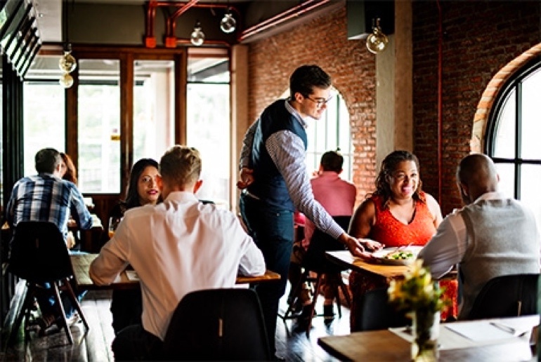 Waiter serving a dish inside a restaurant to a smiling couple