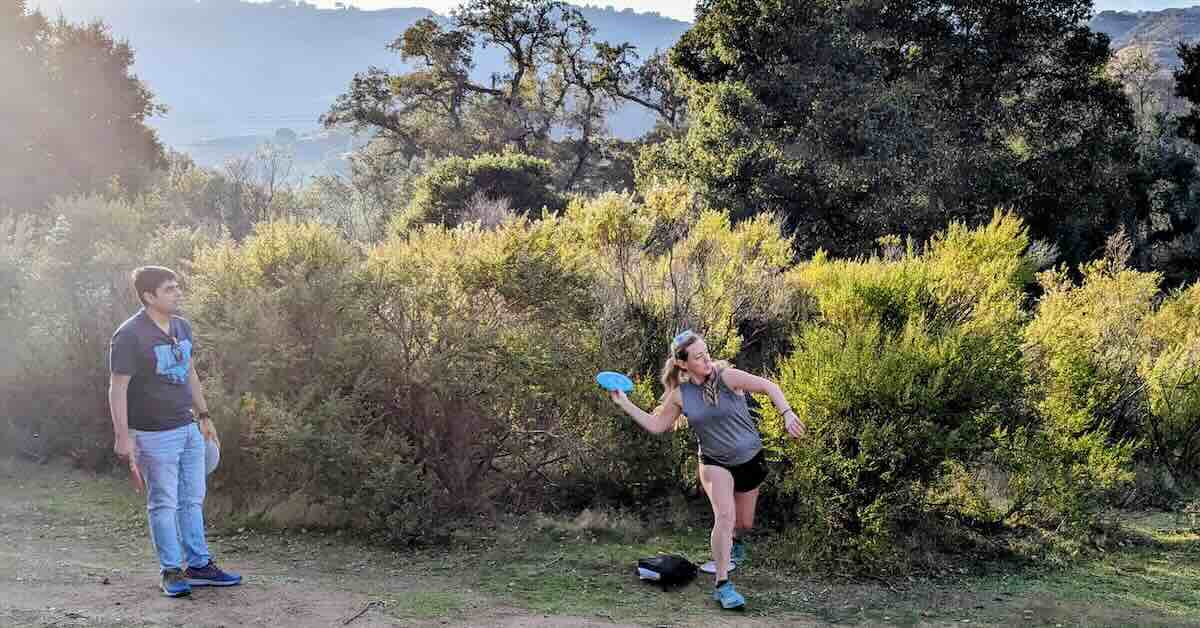 A woman leaning out to throw a forehand disc golf shot in afternoon light