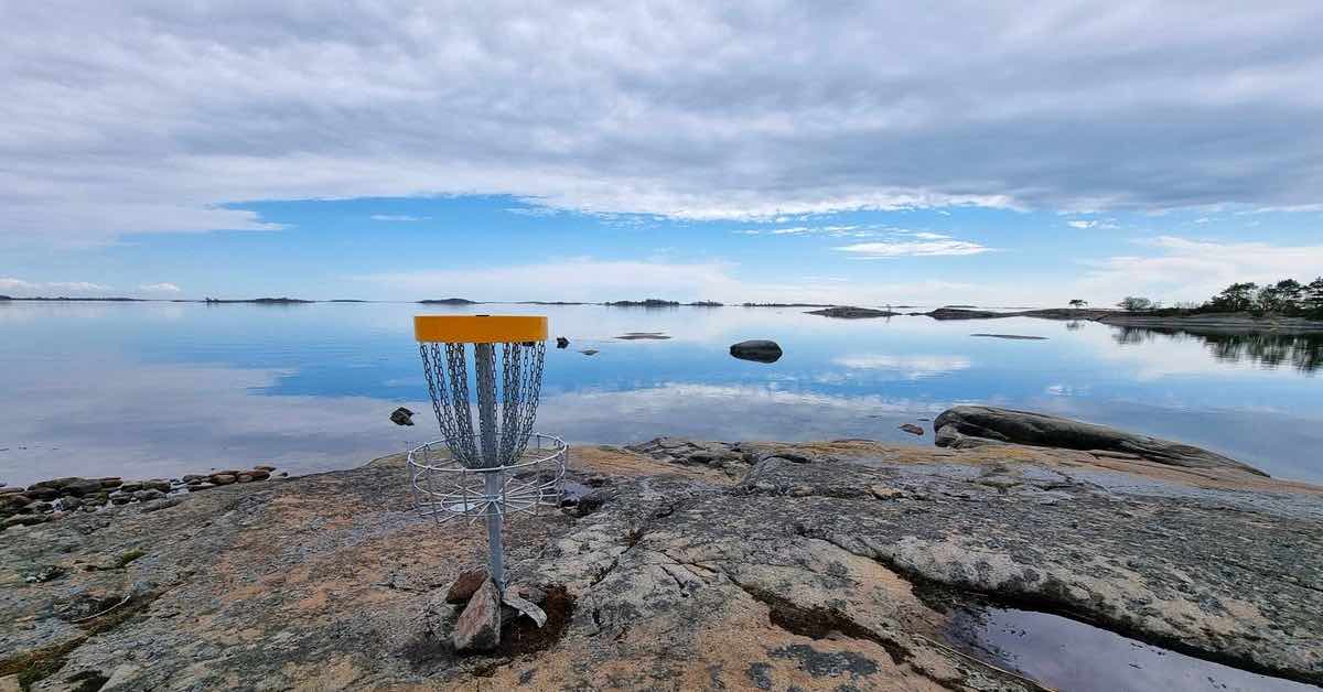 A disc golf basket on rock near a large body of salt water