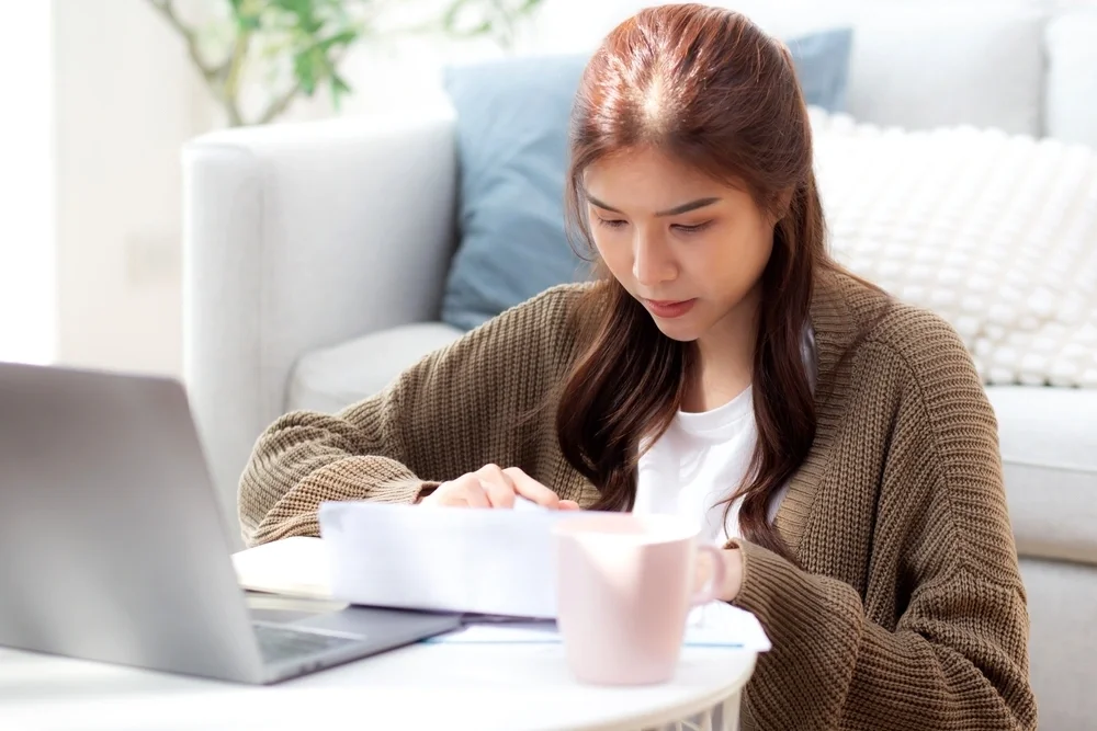 Woman looking at paperwork with her laptop open