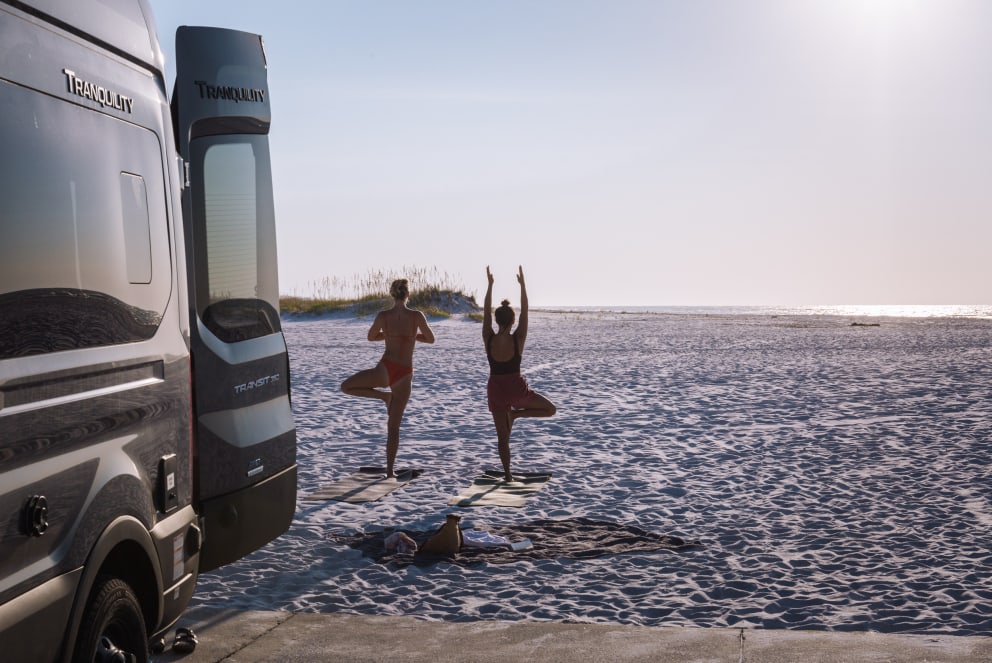 friends doing yoga outside campervan on the beach