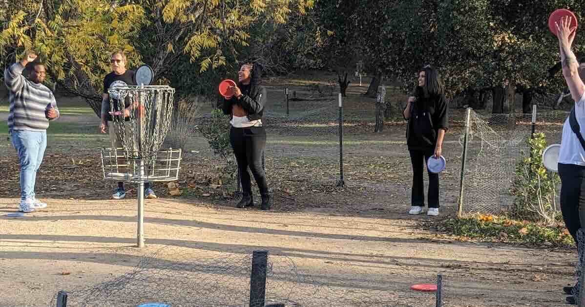 People celebrating and clapping near a disc golf basket