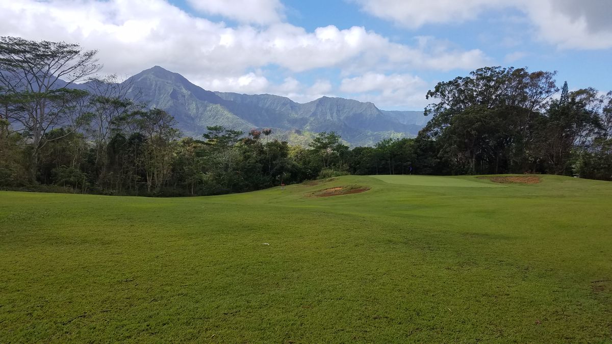 A well-groomed golf fairway with mountain covered in tropical vegetation in the distance
