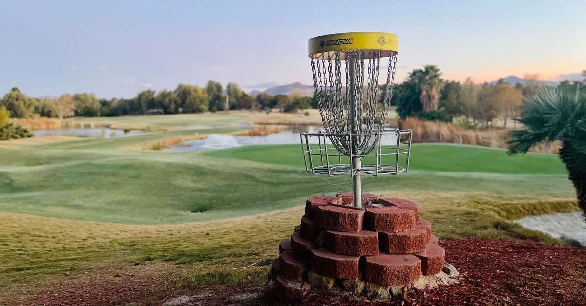 Disc golf basket with base surrounded by red bricks and golf course landscape in the background