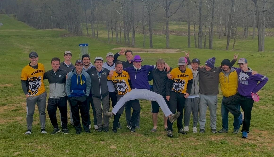 A group photo of disc golfers outside in purple and yellow college gear