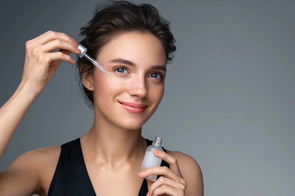 A young woman applying a serum to her cheeks
