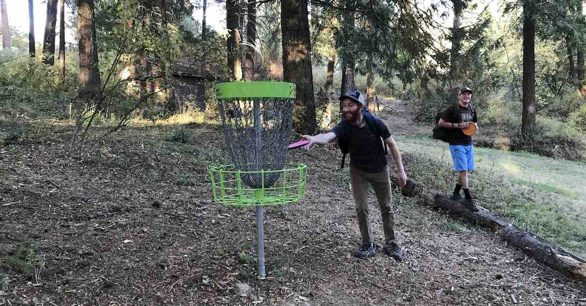 Two men playing disc golf. One putts