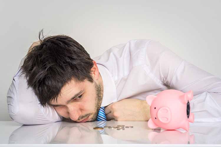 man worried with head on the desk and tipped over piggy bank
