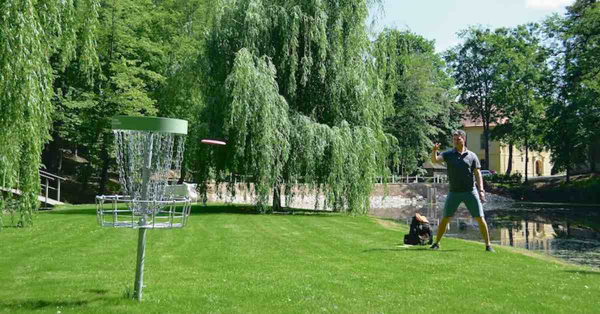 A disc golf basket on a pebbly bank near a flowing stream