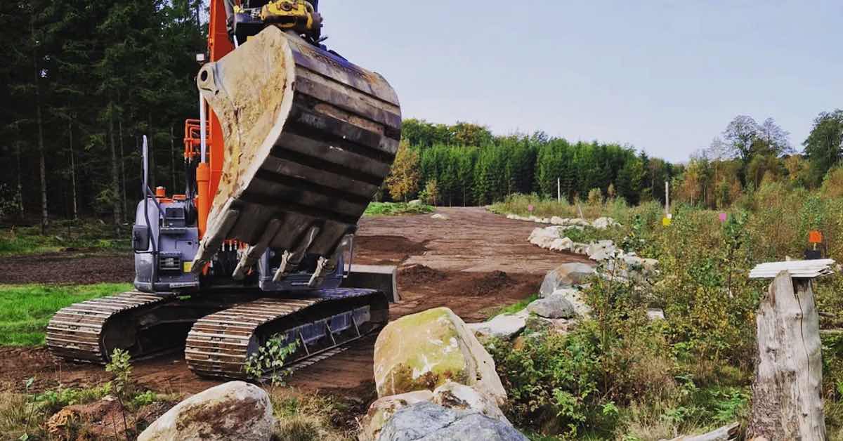 A alrge excavator in front of a smoothed area of dirt in a rural setting