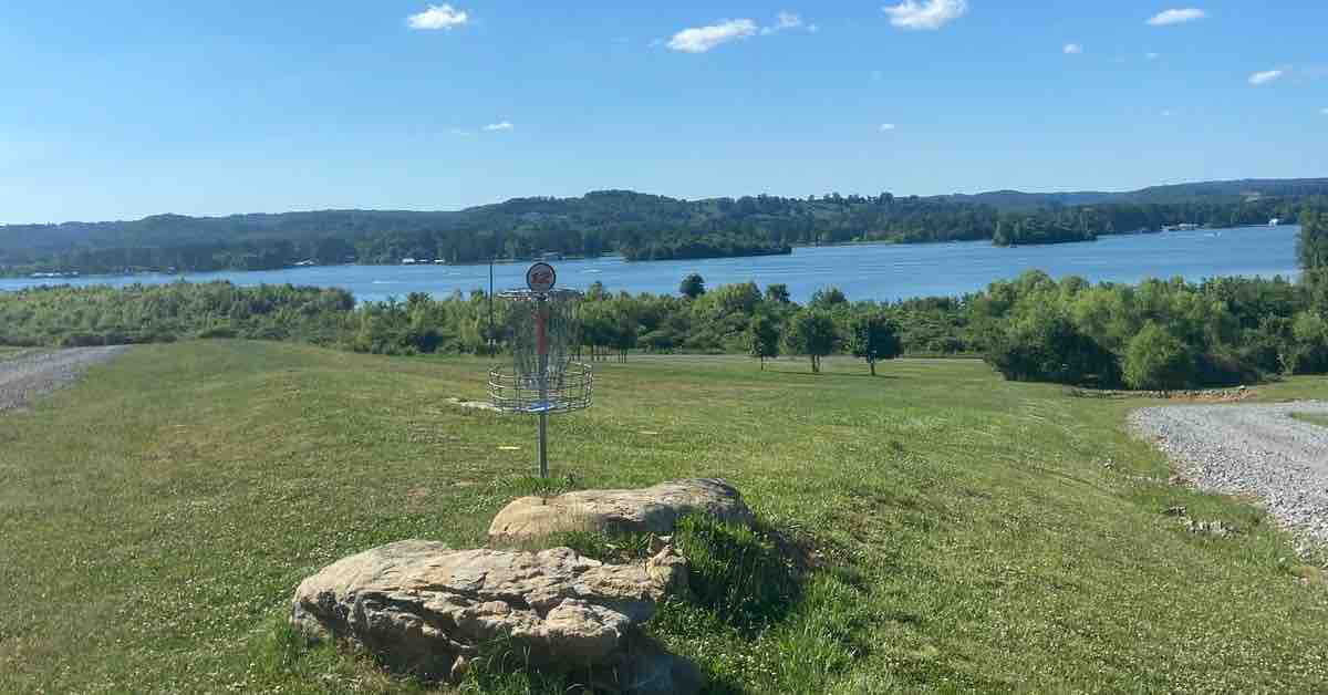 A disc golf basket in the foreground with a lake view behind