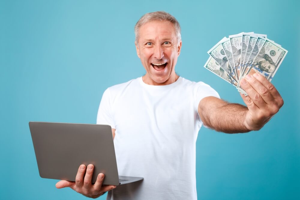 happy man that is holding payday loan cash in hand and laptop in the other