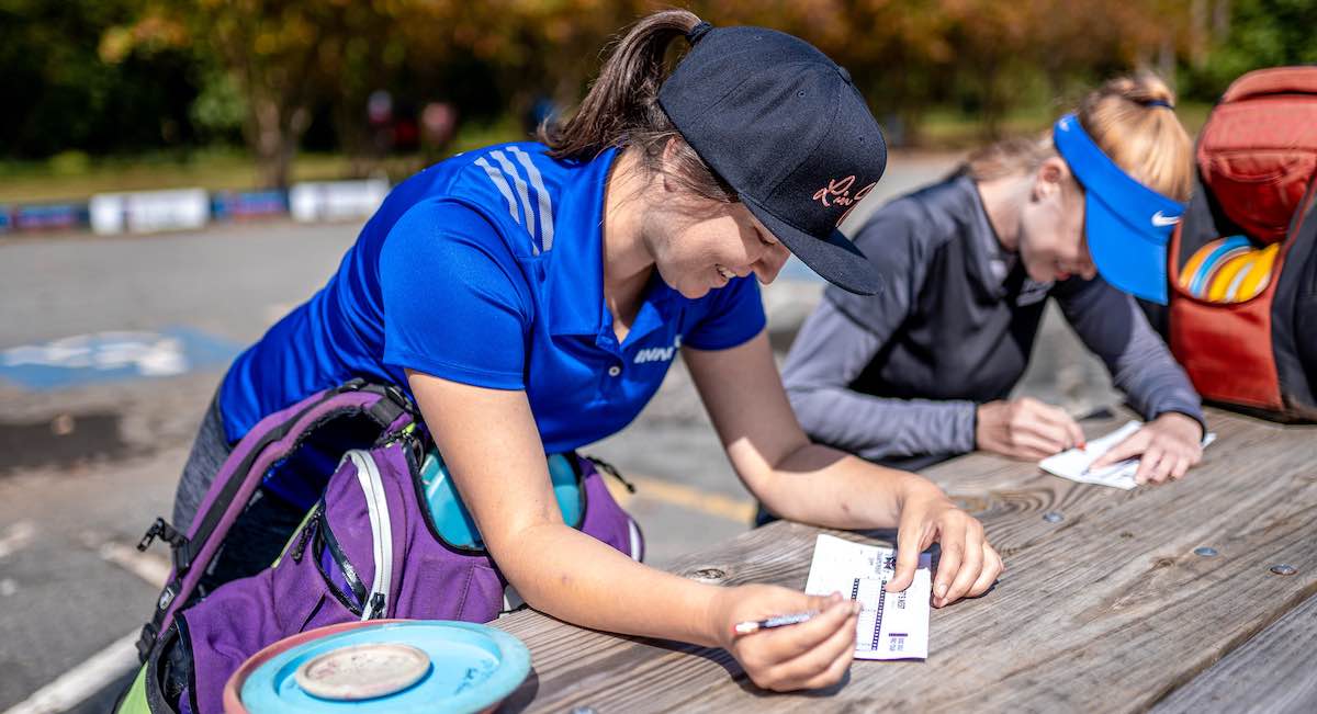 Two women fill out scorecards at a picnic table