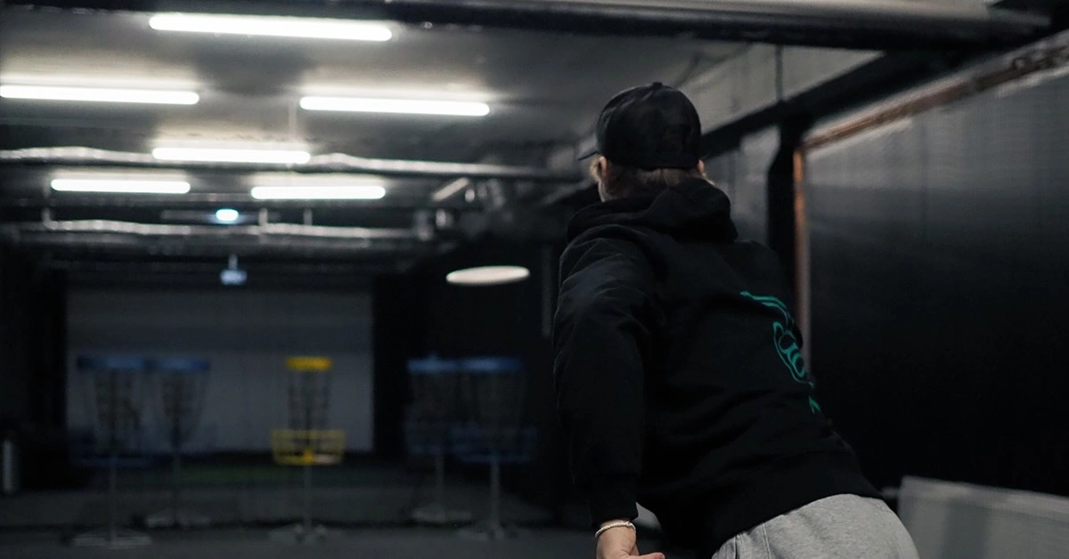 A young man in a black hoodie puts at disc golf baskets indoors