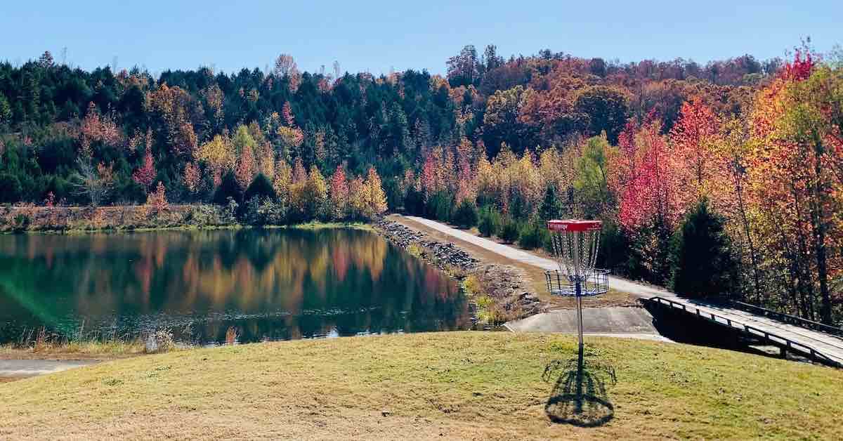 A disc golf basket on an elevated area with water and woods in fall colors in the background