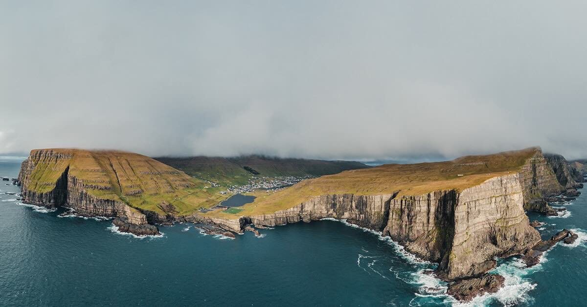 Aerial photo of an island dramatically rising from the ocan with stone cliffs covered in green grass