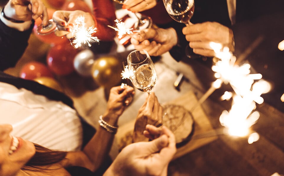 Several hands holding sparklers and wine glasses and sparklers