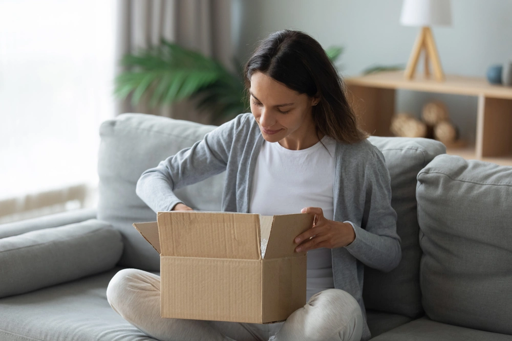 Young woman sitting on couch unpacking cardboard box