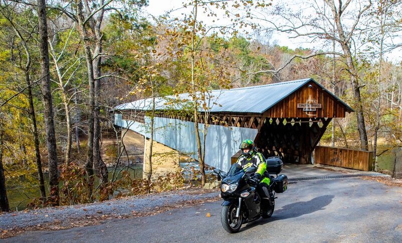 Motorcyclist in front of covered bridge.