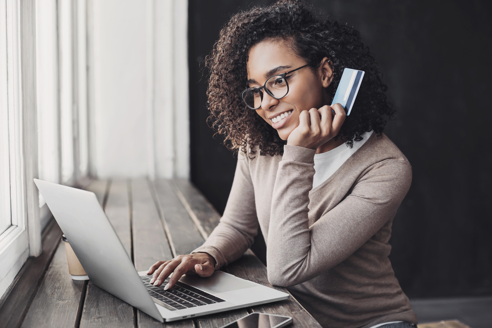 Happy woman holding payment card using a laptop