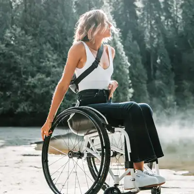 Woman in a wheelchair overlooks forest lake.