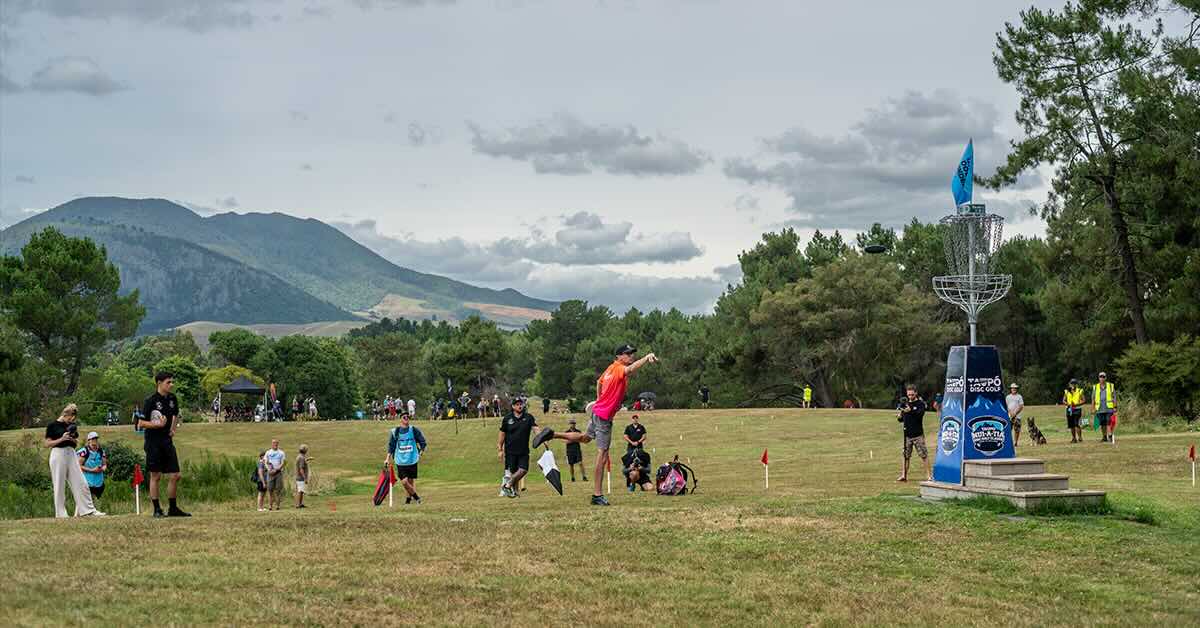Man putts a disc at an elevated basket during a tournament