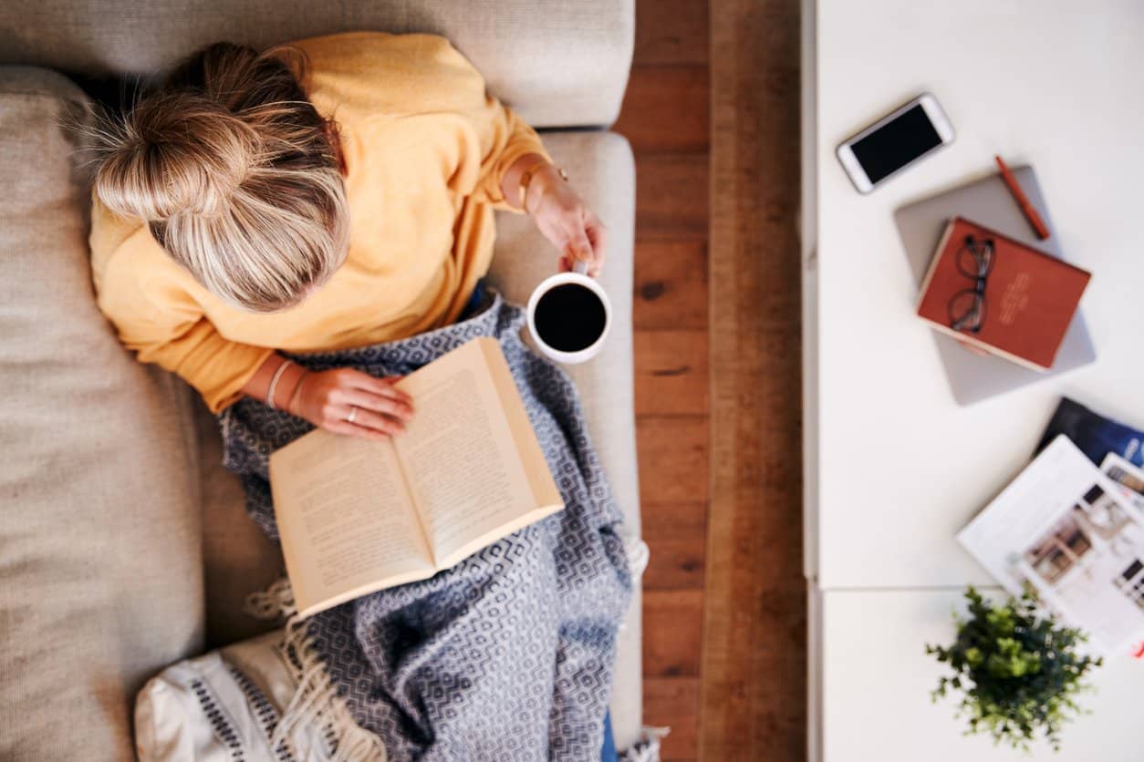 top view of a female laying on the couch reading a book