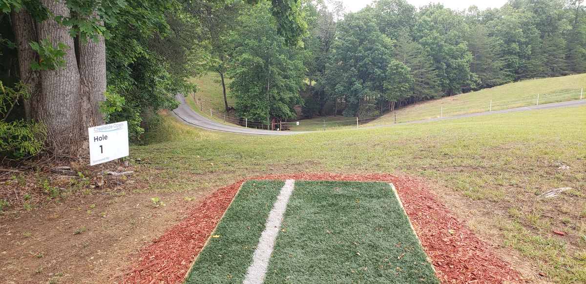 A turf tee pad leading to a very downhill disc golf fairway