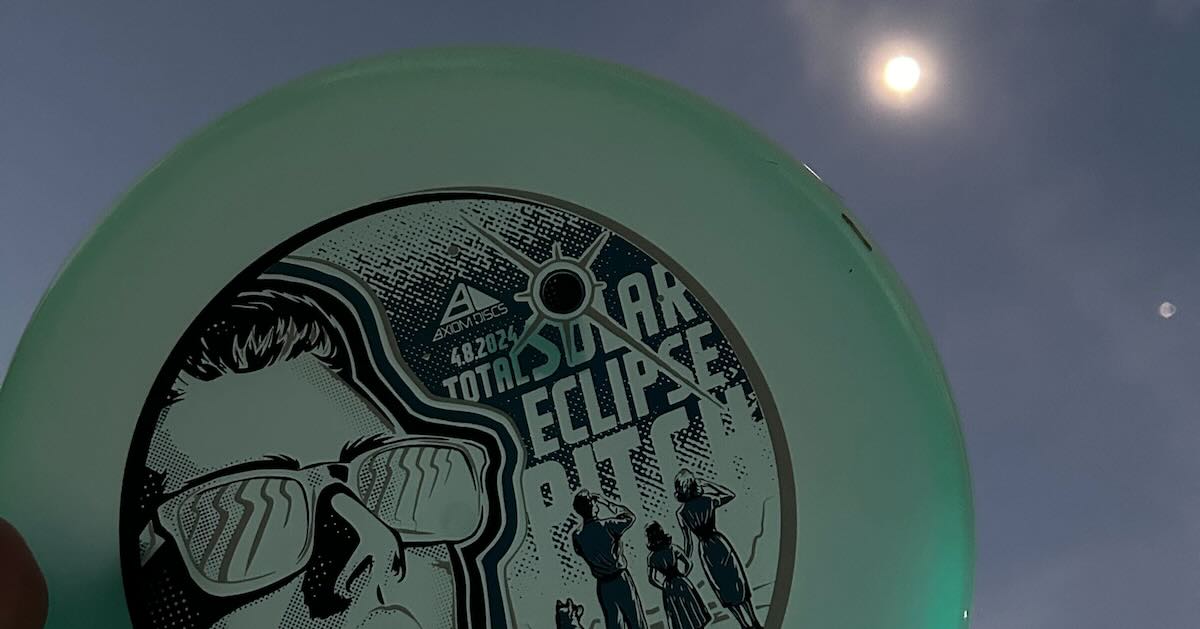 A light blue disc with graphics of people looking at an eclipse help up to the sun