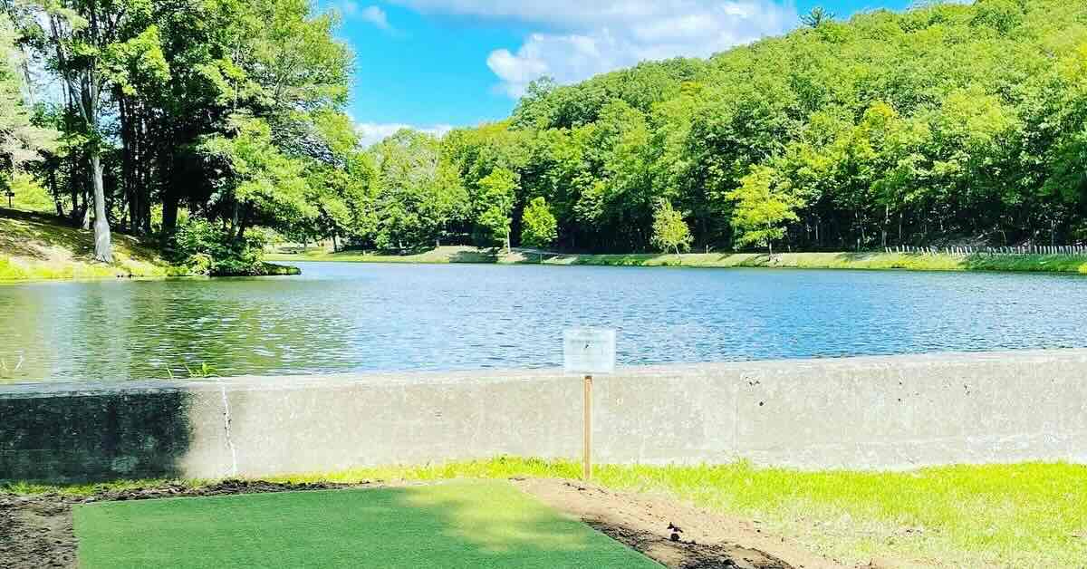 A turf disc golf tee pad in front of a lake