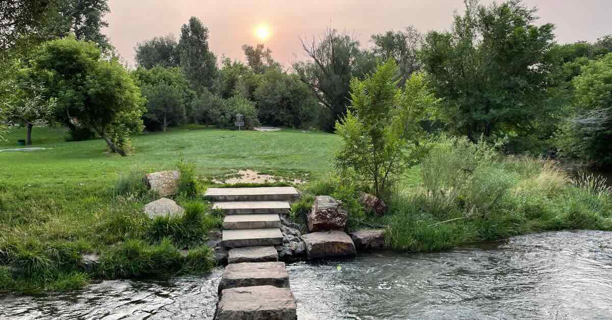 Large stones create a path over a stream to a disc golf green in a park setting