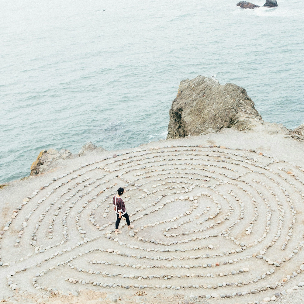 Woman explores a rock maze by the ocean.