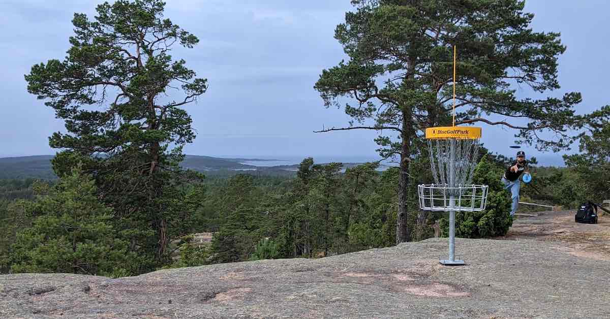 A disc golf basket on a stone ledge with a person putting at it