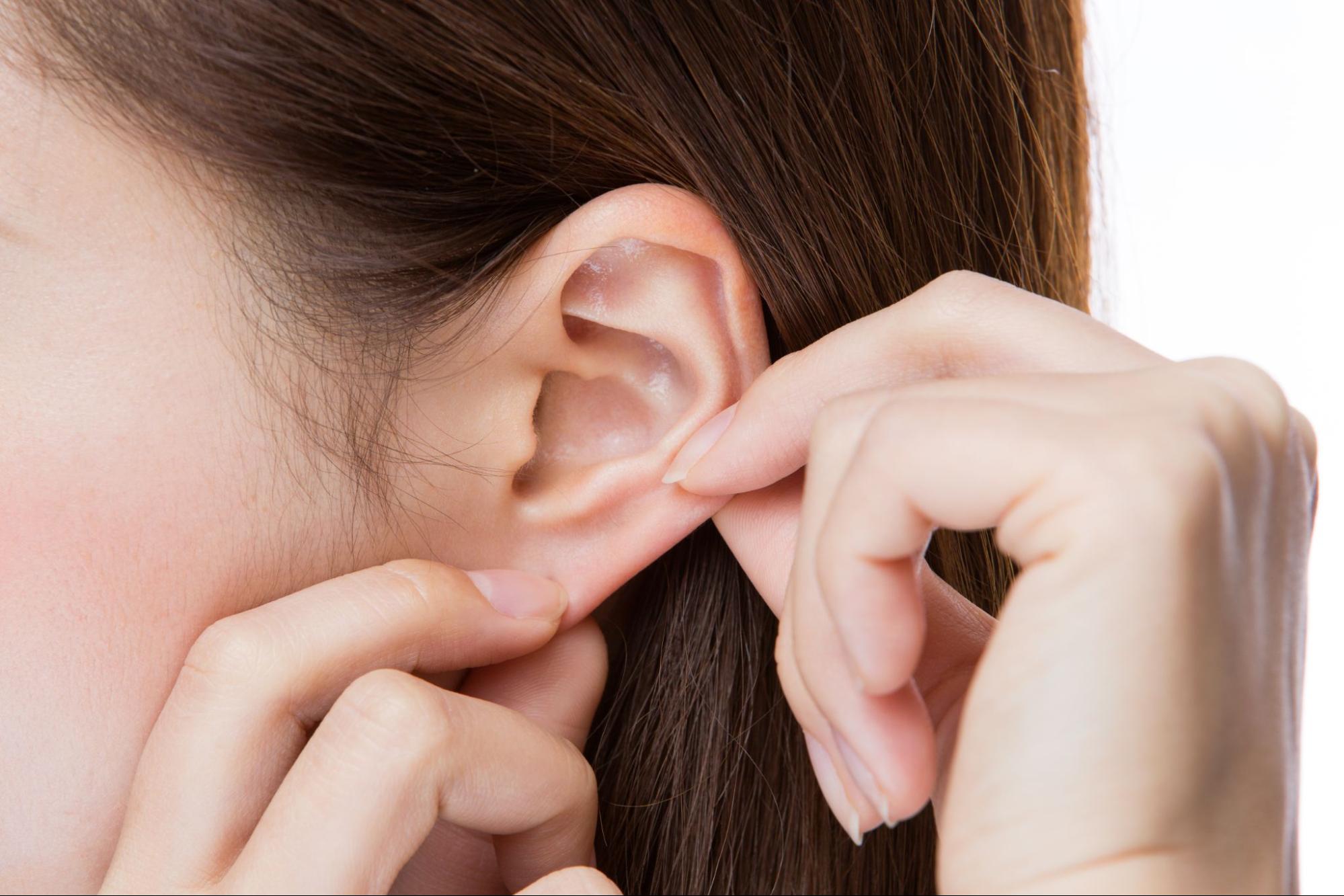 how to clean your ears: Close up shot of a woman holding her ear with her fingers