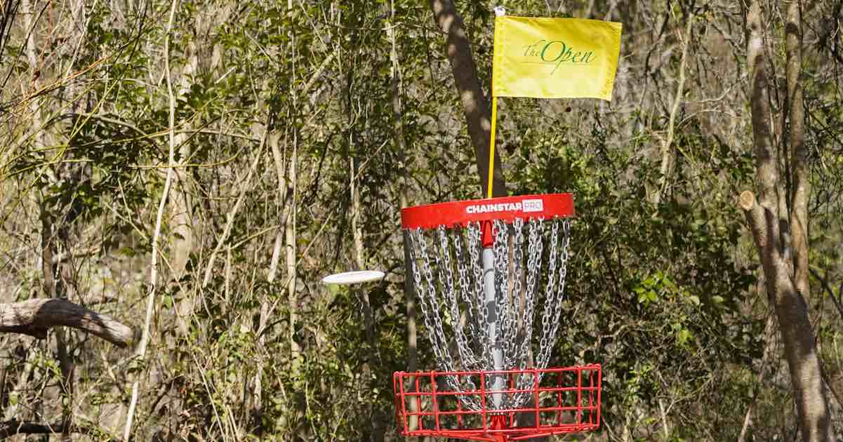 Red disc golf basket with a disc flying toward it and a yellow flag on the top with the text 'The Open' written on it