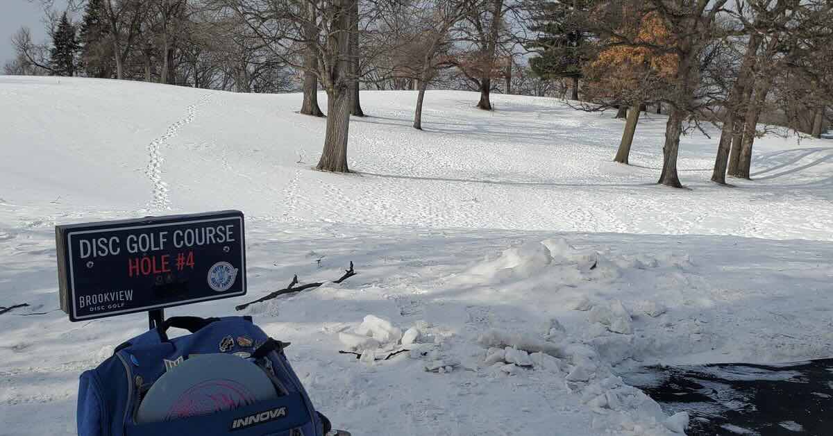 A disc golf tee sign in a snowy area with scattered trees