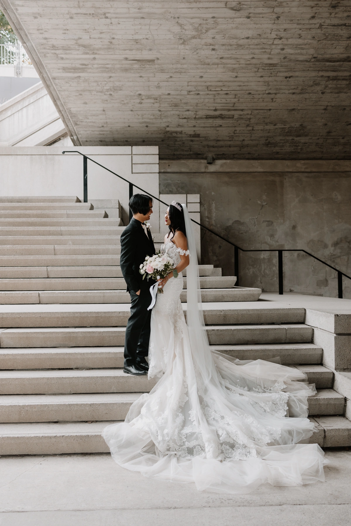 Bride and groom on steps with the bride holding a bridal bouquet and white wedding dress flowing over the steps below.
