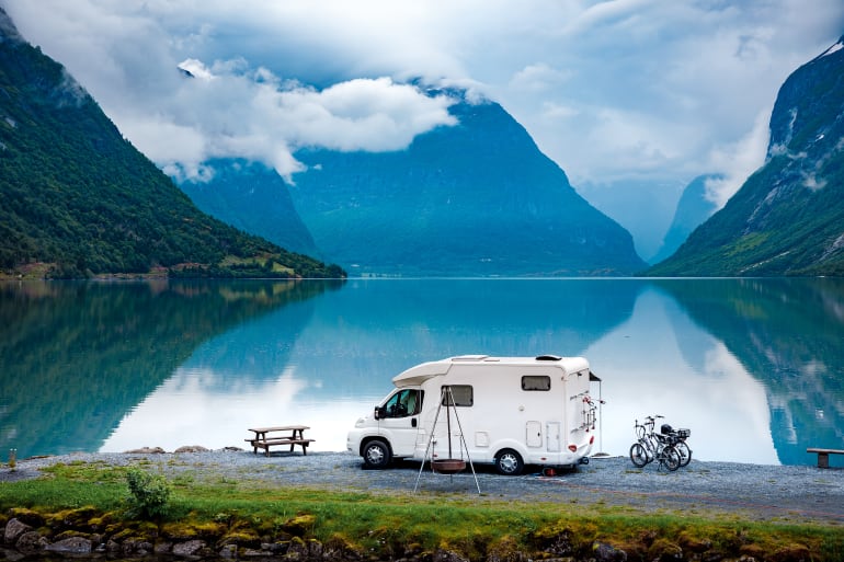 RV parked on side of road in front of lake and mountains