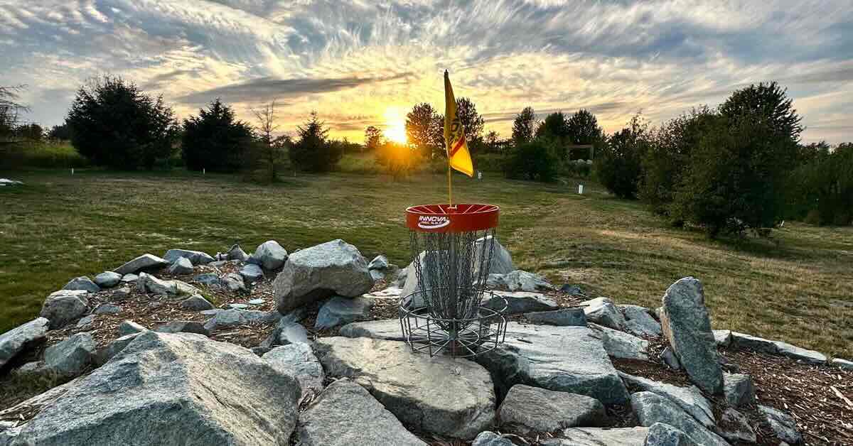 A red-banded disc golf basket surrounded by rocks with swirling clouds in the sky