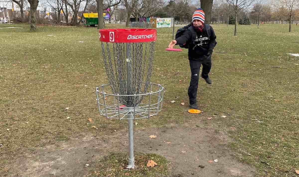 Man in winter clothes putting at a disc golf basket from short range