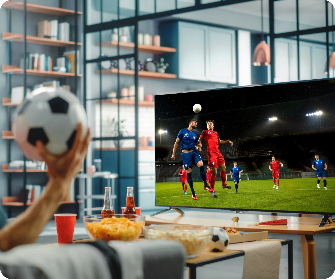 Person holding football while streaming a live match on their smart TV.