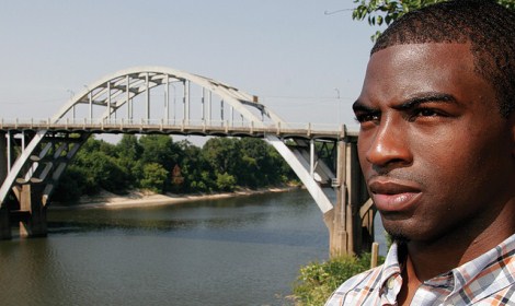 Man staring with an arched bridge in the background over a river