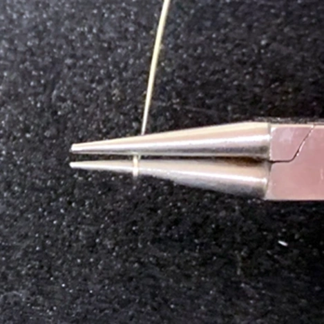 looping end of silver wire around round nose pliers 