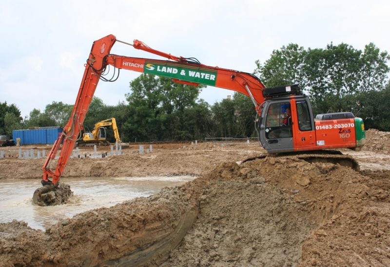 Hitachi long-reach excavator digging dirt from a flooded area with another excavator in the back