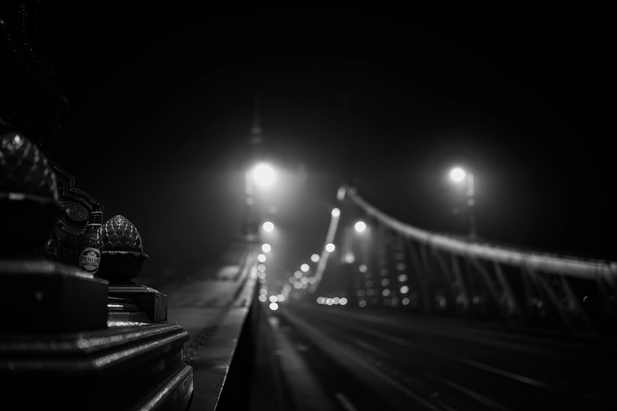 A low-angle view of a bridge lit up by streetlights at night, with a soft focus on the foreground and the bridge fading into the background.