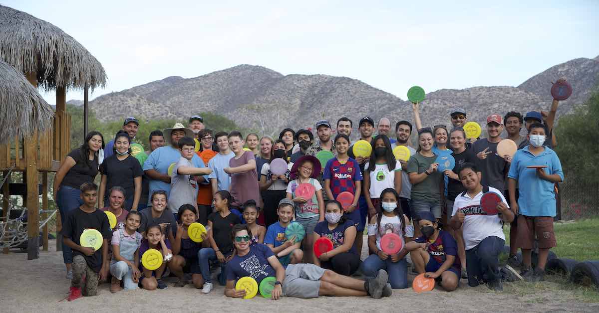 A group of some adults and mostly kids holding discs and posing fro a group photo