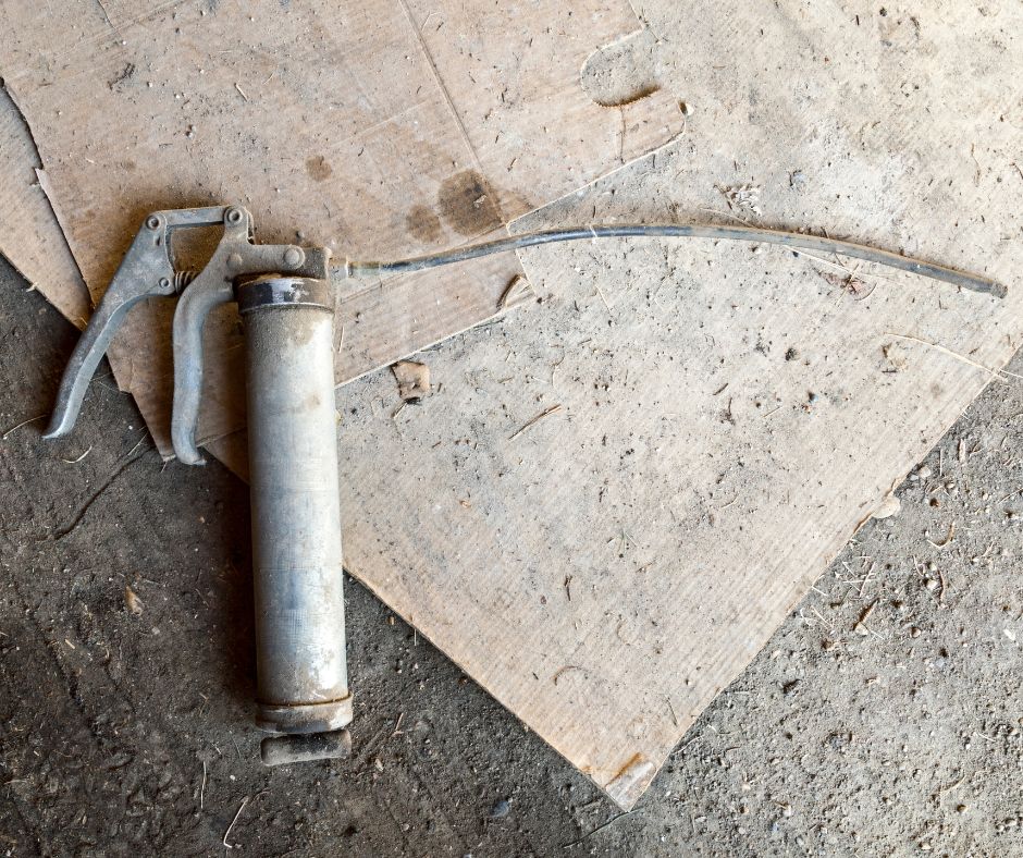 A grey, dusty manual grease gun lying on the ground