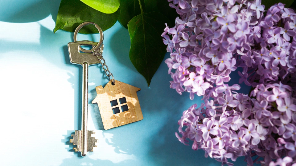 House key with keychain on blue spring background and lilac branches.